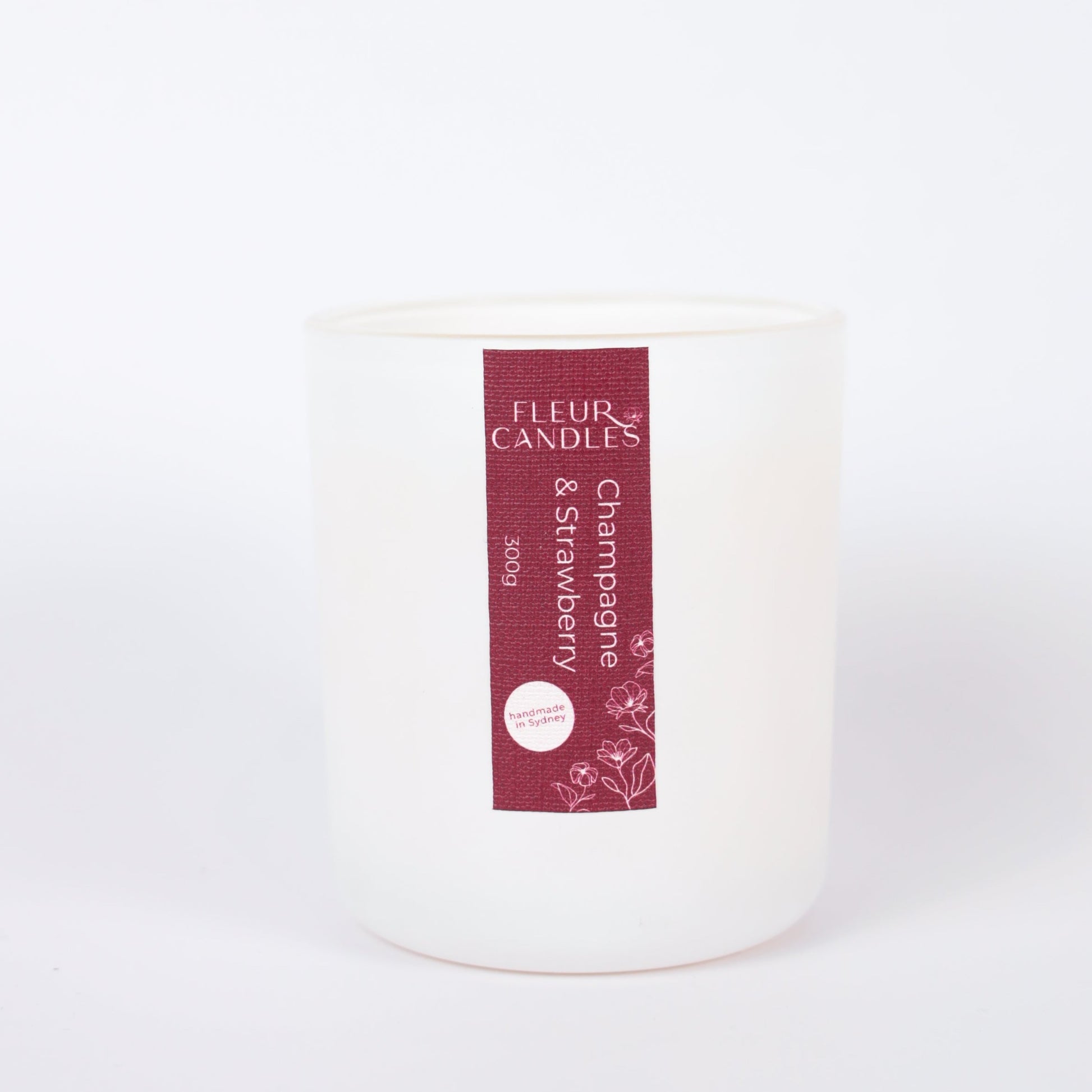 white candle with burgundy label on a white background. fragrance is "champagne & strawberry"