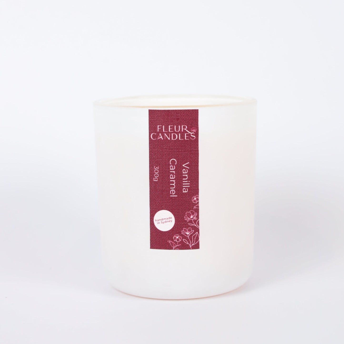 white candle with burgundy label on a white background. fragrance is "vanilla caramel"
